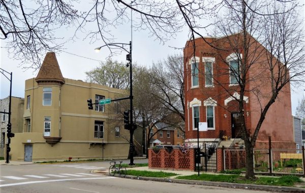 A tour bike standing at a quiet intersection with two late nineteenth century buildings, one a red brick Italianate the other tan sided Queen Anne with shingled corner turret on each corner