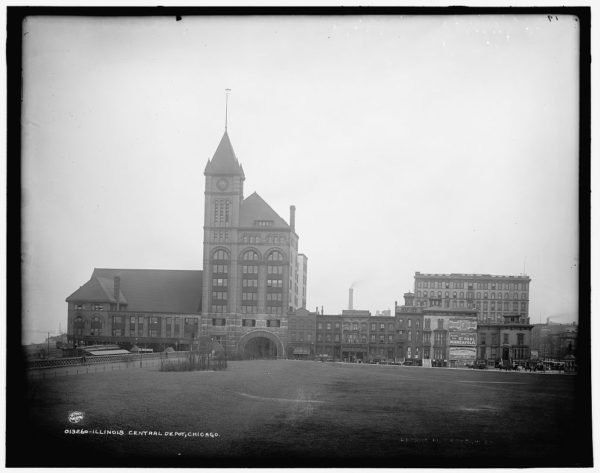 A historical black and white of a limestone train station with point capped tower sitting in an wide expanse