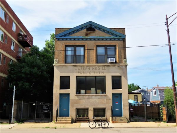 A tour bike standing at the curb in front of a two story stone facade with Joseph Medill Public Bath epigram.