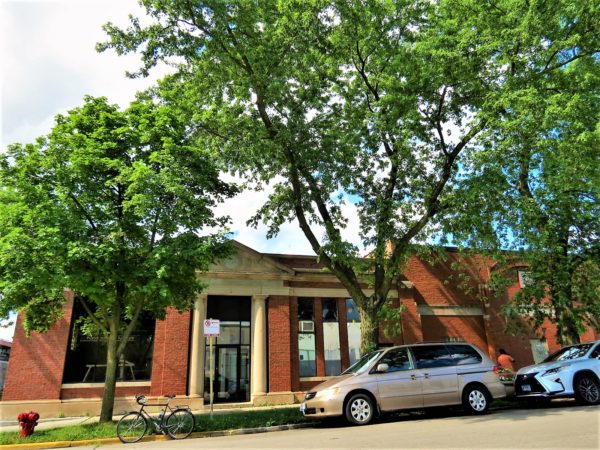 A tour bike standing at the curb in front of a one story red brick and limestone Classical Revival entry way former post office.