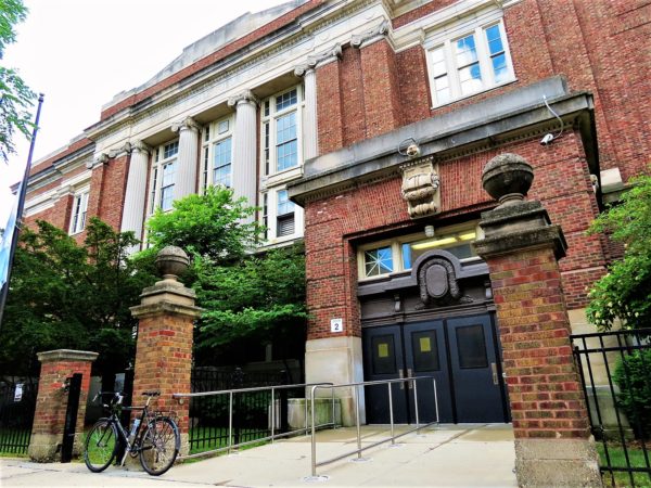 A tour bike leaning on a brick pillar of the entry walkway into a red brick and limestone detailed Classical Revival four story school