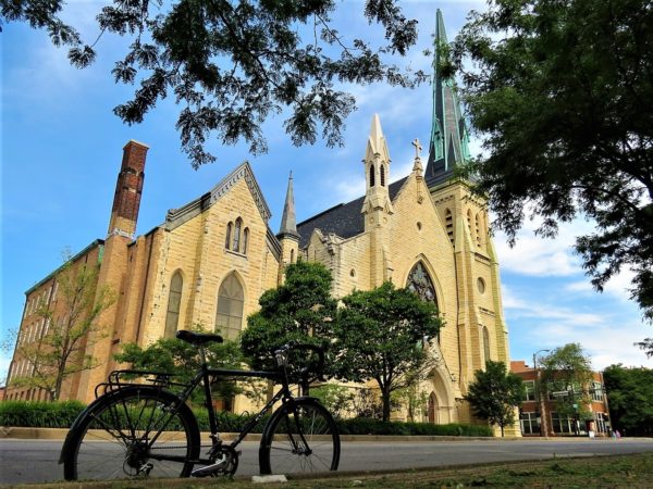 A tour bike standing across the street from a yellow limestone Gothic Revival church.