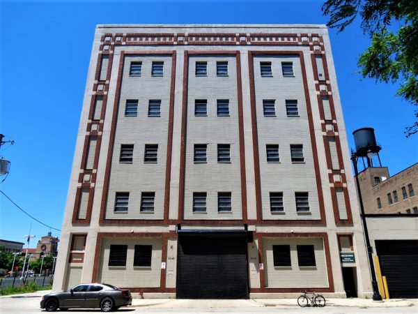 A tour bike standing at the curb in front of a five story early 20th Century storage warehouse with a brickwork design facade.