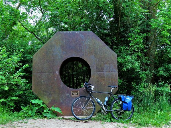A tour bike standing in front of a dark brown metal sculpture of a large hardware nut.