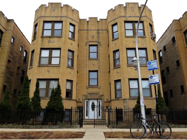 A tour bike standing in front of a three story yellow brick early 20th Century apartment building.