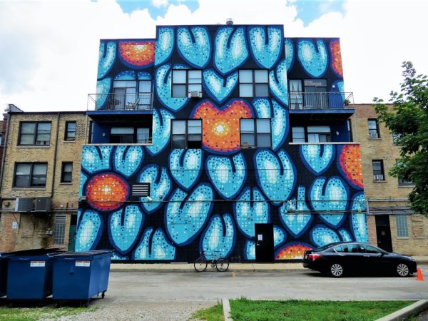 A tour bike leaning on a large three story mural of orange fruit and light blue leaves on a dark blue background.