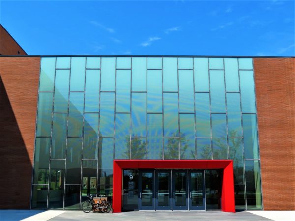 A tour bike leaning to the side of a red metal rectangular entry into a glass wall.