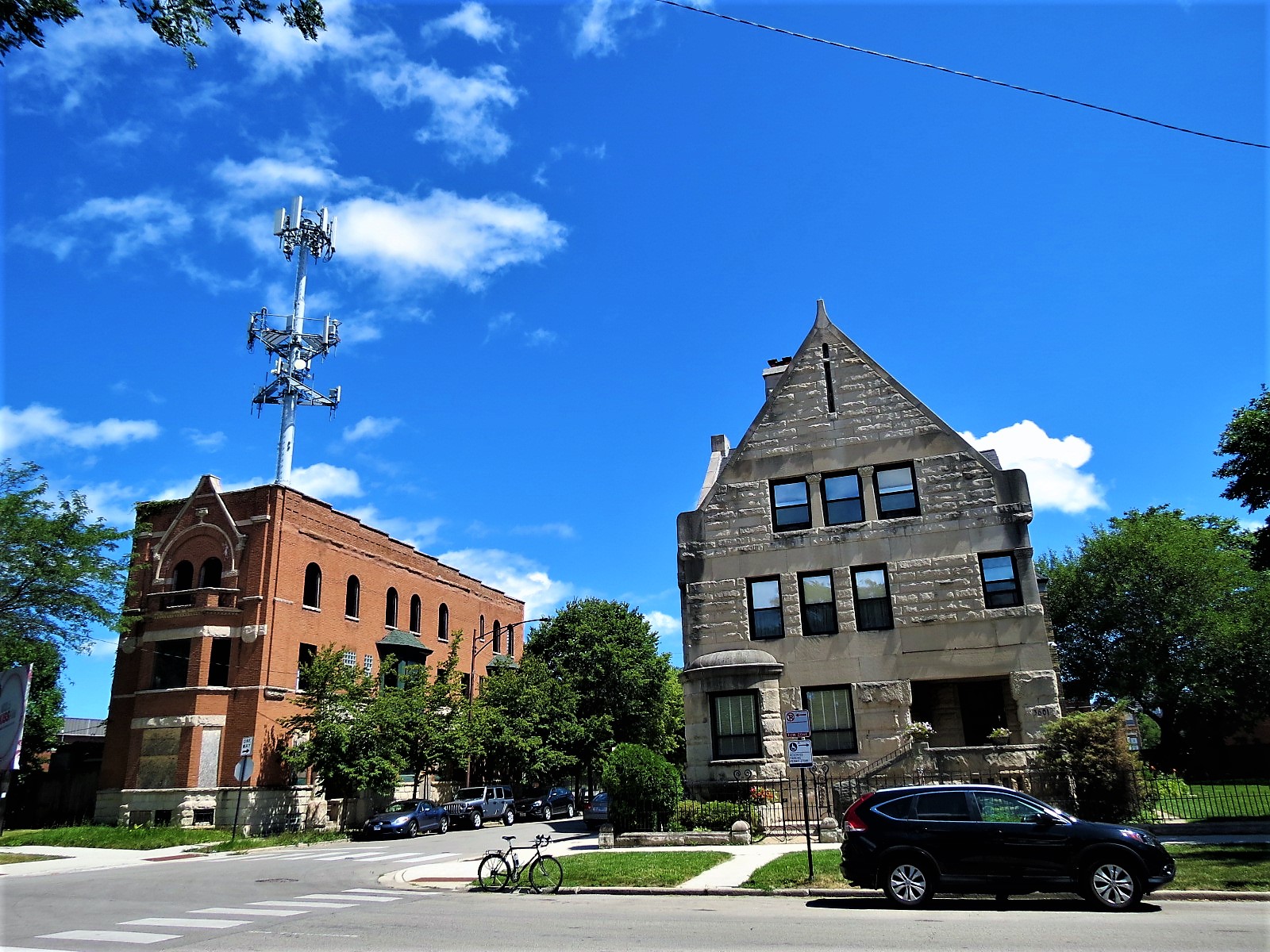 A tour bike at the curb in front of high pitched three story grey stone sitting across the street from a red brick windowless three flat with a front bay window.