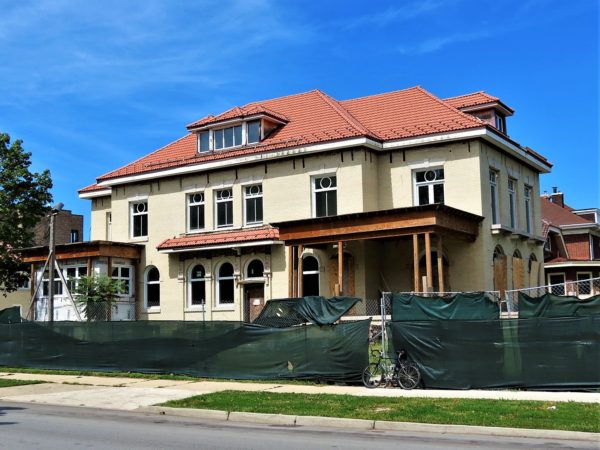 A tour bike leaning on a green cloth coveed construction fence around a three story early 20th Centrury low hipped roof three story undergoing renovation