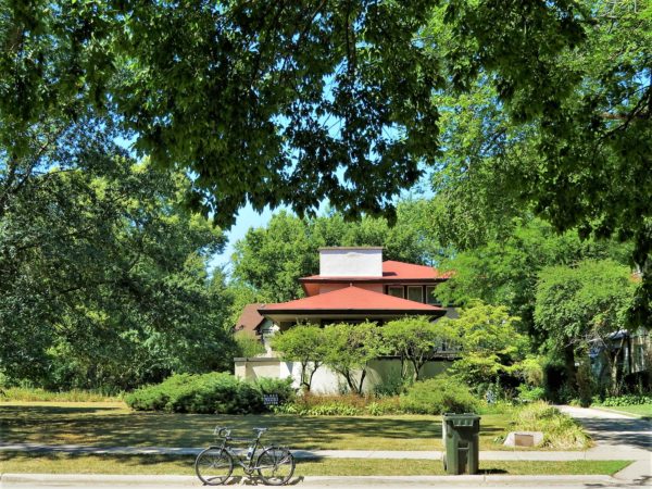 A tour bike standing at the curb with low hipped red home roofs framed by the trees around it and in he foreground.