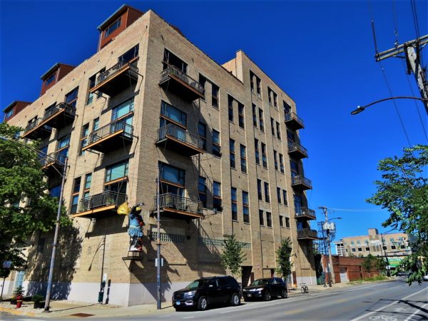 A tour bike standing at the curb below four story common brick loft space with black metal balconies and fire escapes..