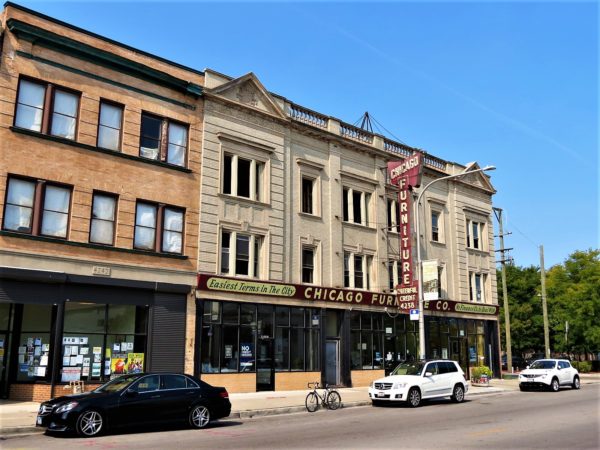 A tour bike at the curb in front of a three story Classical Revival storefront with a maroon vintage vertical metal and light bulb sign.