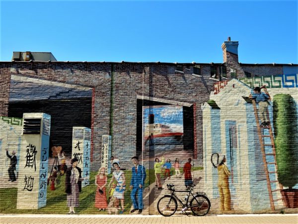 A tour bike leaning on a mural depecting the history and diverse ethnic character of the surrounding neighborhood.