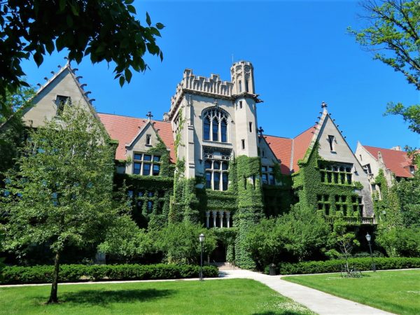 A tour bike standing in the grass infront of a green ivy covered Gothic Revival three story stone building with three gables and a center tower.