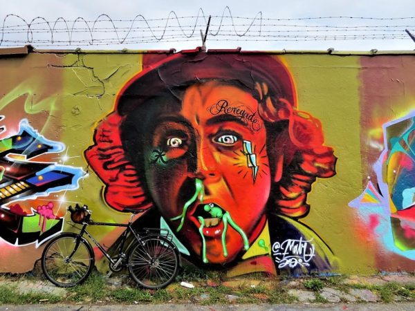 A tour bike leaning on a mural of an off color zombie like Gene Wilder as Willy Wonka