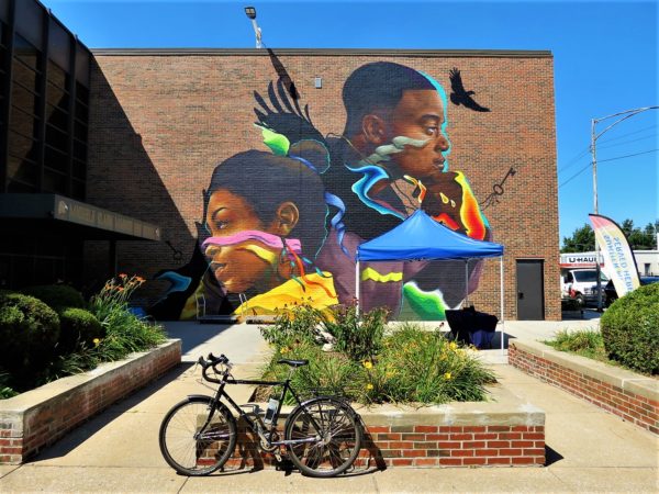 A tour bike standing in front of a colorful  Afro futuristic style mural of two Black teenagers. one boy one girl.