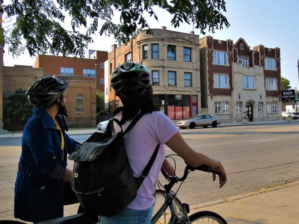 Two CBA bike tour riders looking at a three story red brick building with a limestone Classical Revival facade.