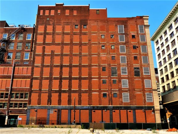 A barely visible tour bike at the base of a nine story mostly bricked window building