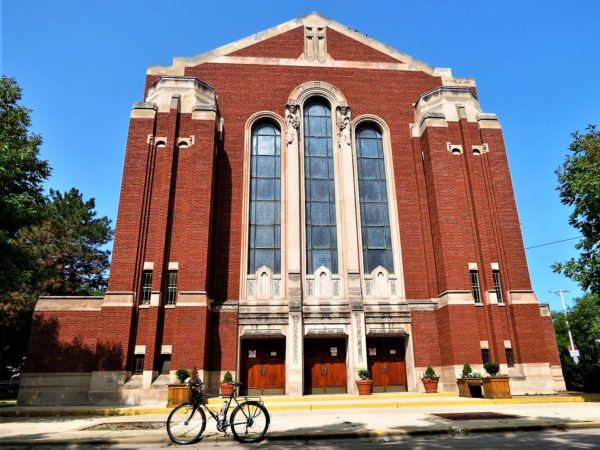 A tour bike at the curb in front of an Art Deco red brick and limestone detailed church