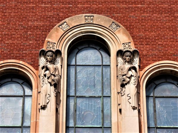 Two limestone angels on either side of an limestone arched window with Christian symbols.