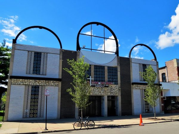 A tour bike in front of a Mid Century Modern two story with a facade of fake stone and brown and glass bricks and framework remains of circular signs on the roof.