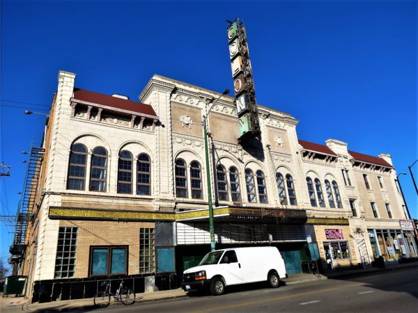 A tour bike in front of a Moorish Revival terra cotta theater façade with an aging Colony sign of individual letters vertically.