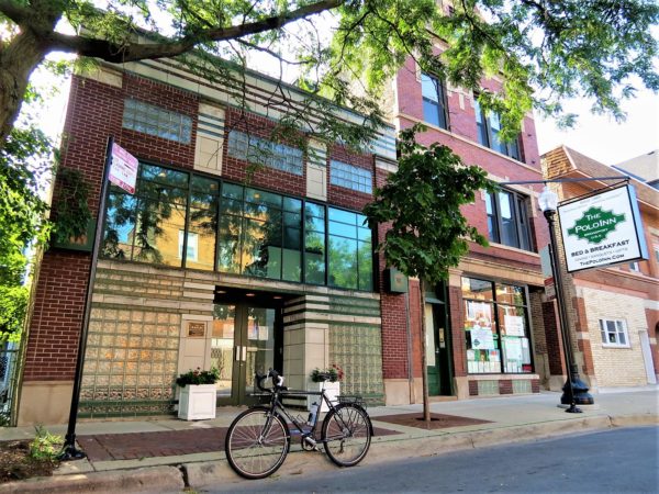Under a tree canopy a tour bike in front of a two story red brick and cream terra cotta accented three story former theater building.