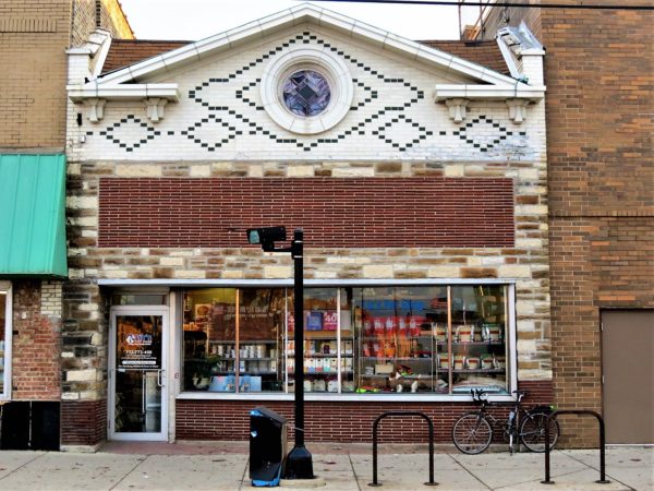 A tour bike leaning on a one and half story green and white glazed brick storefront with an oculus in the pediment.