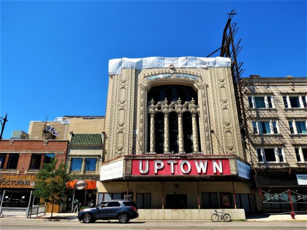 A tour bike in front of a terra cotta covered grand entrance to a decaying closed movie theatre with a large metal and light bulb Uptown sign.