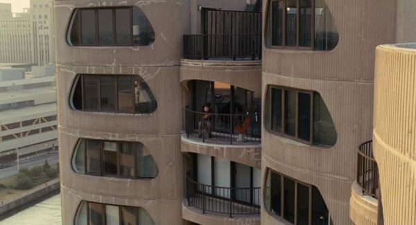 A movie still of Will Ferrell sitting on the balcony of the space age Brutalist River City