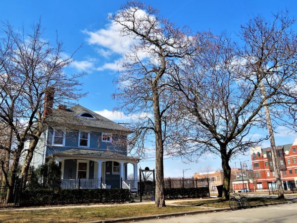 A tour bike standing in front of a light blue and white trim painted three story wood 1880s home with an open field at the right.