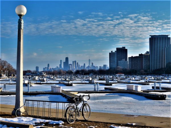 A tour bike looking out over a frozen harbor with the high rise apartments near and the Chicago skyline in the far distance.
