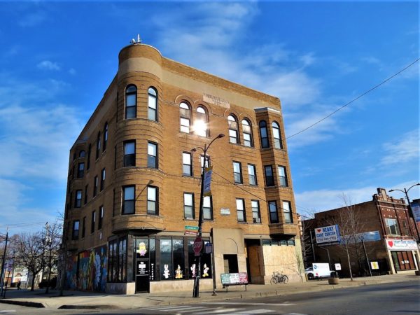 A tour bike leaning at the base of a four story tan brick corner turreted building.