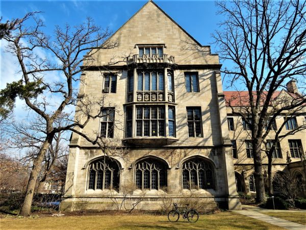 A tour bike standing in front of a Collegiate Gothic building with leafless tress on either side.