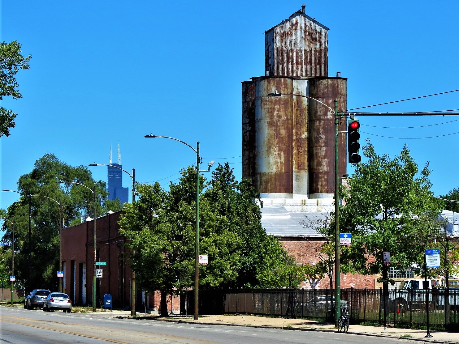 A tour bike standing at the curb with a rusted metal 7 story seed elevator and the Willis Tower in the distance.