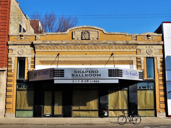 A tour bike standing at the curb in front of a one story yellow brick and limestone and tan brick detailed papered up storefront with metal marquee