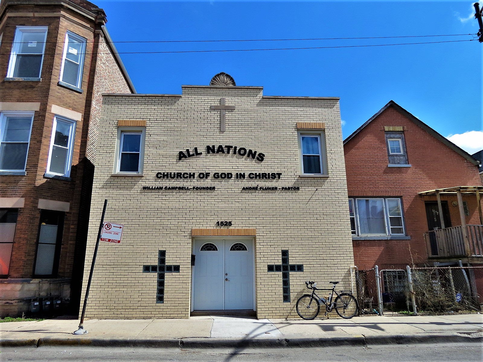 A tour bike standing in front of a two story new yellow brick facade with a center double door flanked by glass block crosses.