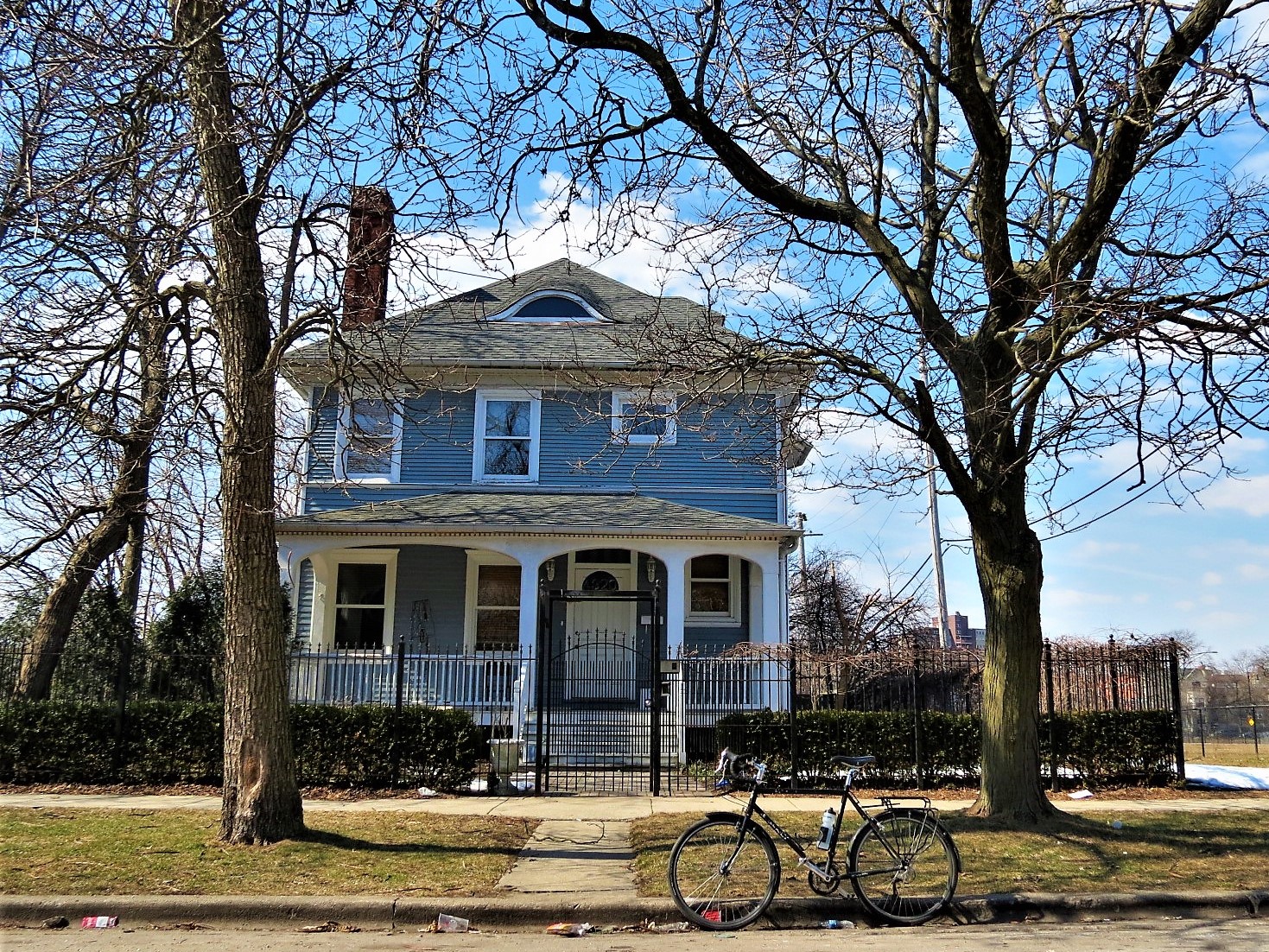 A tour bike standing in front of a pale blue white trim wooden 1880s three story single family home.