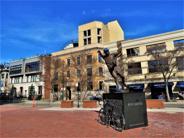 A tour bike leaning on the black marble base of a sculpture of a baseball player throwing a ball.