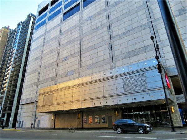 A tour bike standing under a signless Post Modern metal marquee below 5 stories of windowless grey metal and brick building.