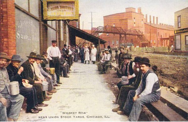 An historical colorized postcard of men sitting on either side of a walkway with drinks in the hands.
