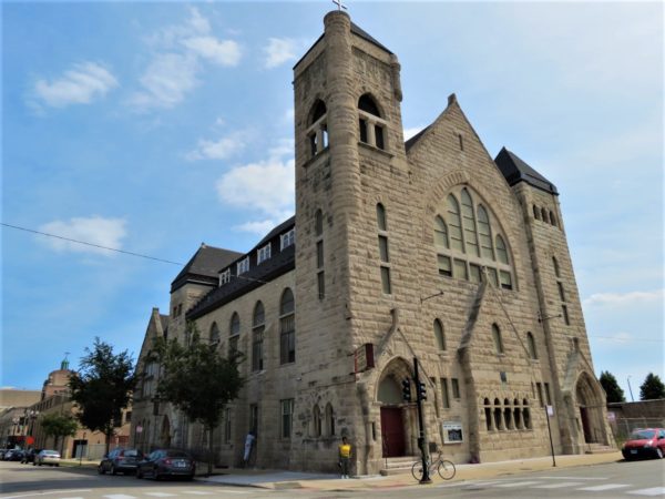 A bike tour rider standing in front of a pale limestone 1890s corner church