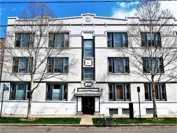 A tour bike standing at front of a three story apartment clad in green& white glazed brick.