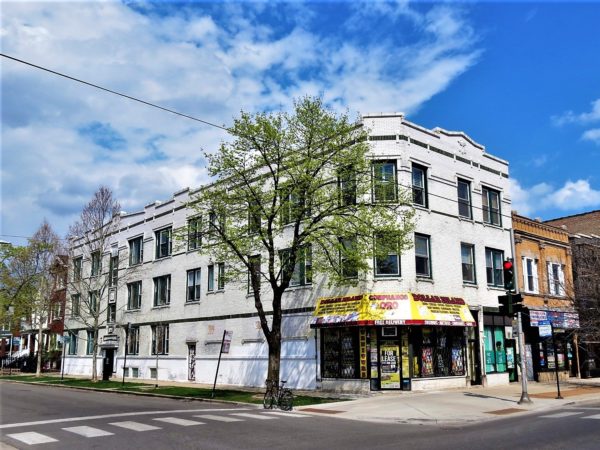 A tour bike at the side of a corner three story storefront and flats clad in green and white glazed brick.