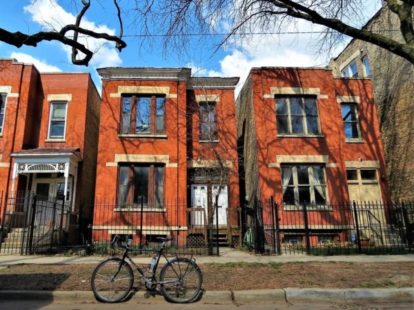 A tpur bike in front of two red brick Italianate two flats with limestone detail..