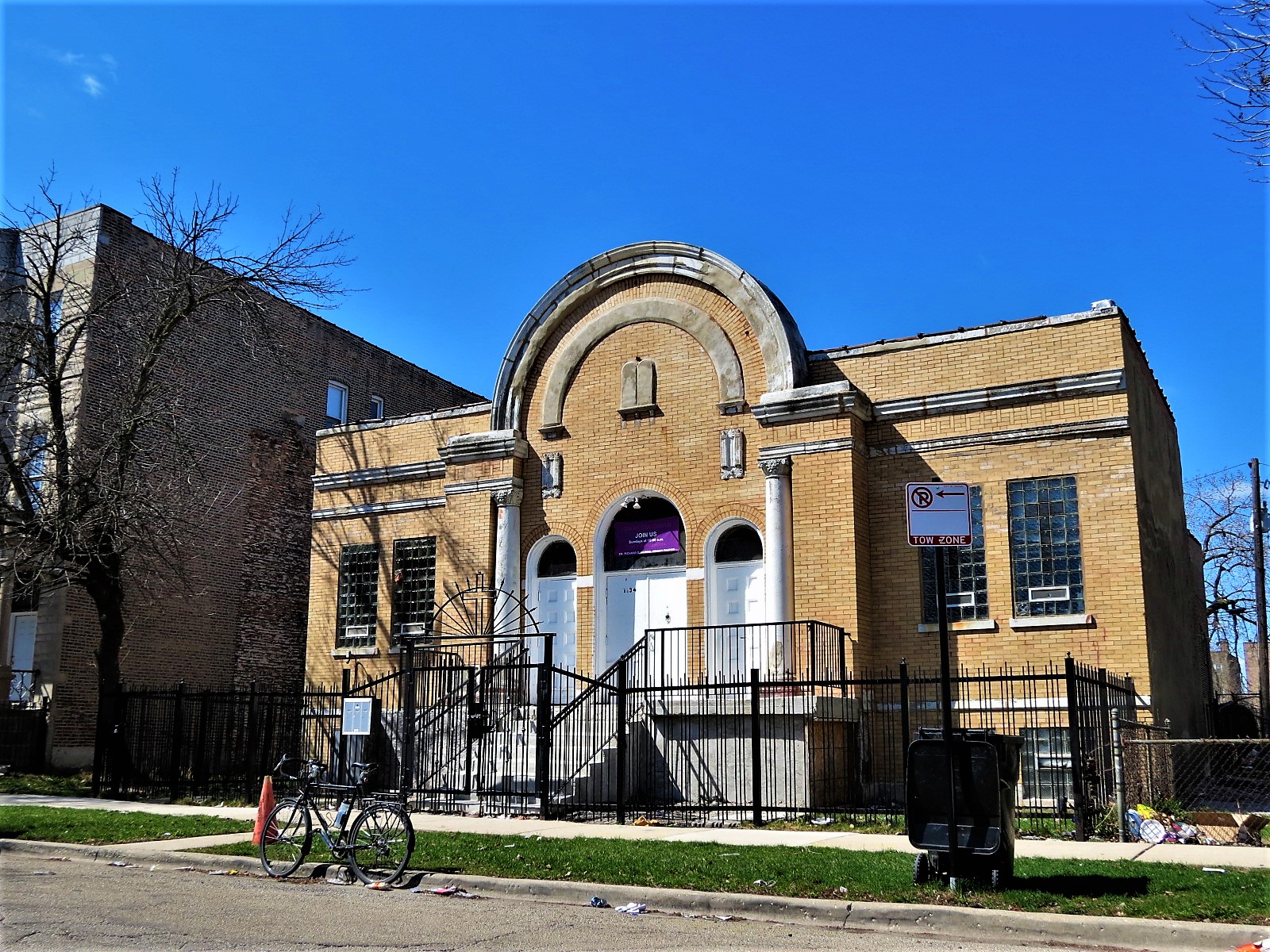 A tour bike standing in front of a yellow brick limestone detailed raised one story former synagogue without rounded center entryway.