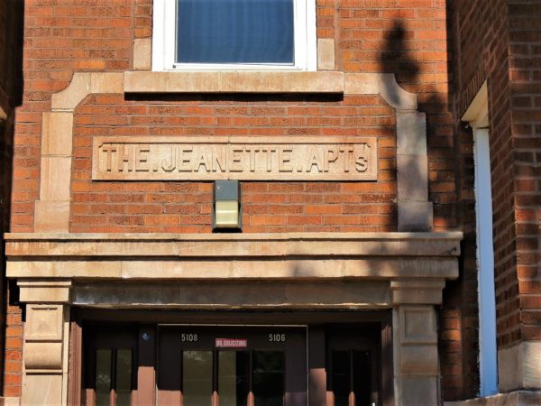 A limestone The Jeanette Apts on brown brick above a Classical Revival limestone entryway.
