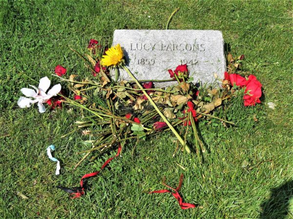 Downward view of a simple rectangular facing up gravestone that reads Lucy Parson with a pile of drying flowers.