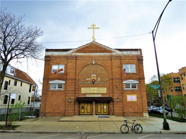 A tour bike in front of a tan yellow three story square mass Classical Revival house of worship.