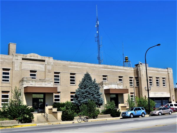 A tour bike in front of a pale yellow brick Art Deco two story public building with three entries and three door garage extending along the road.